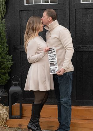 A couple embraces on a wooden deck with a black wall backdrop during a photo session.