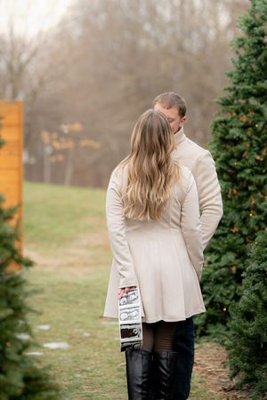 A couple poses together in front of evergreen trees during a winter photo session.