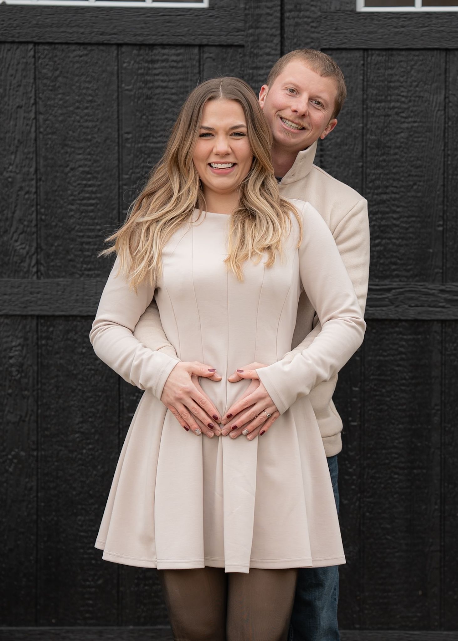 A couple wearing coordinating cream-colored outfits poses against a black wall.
