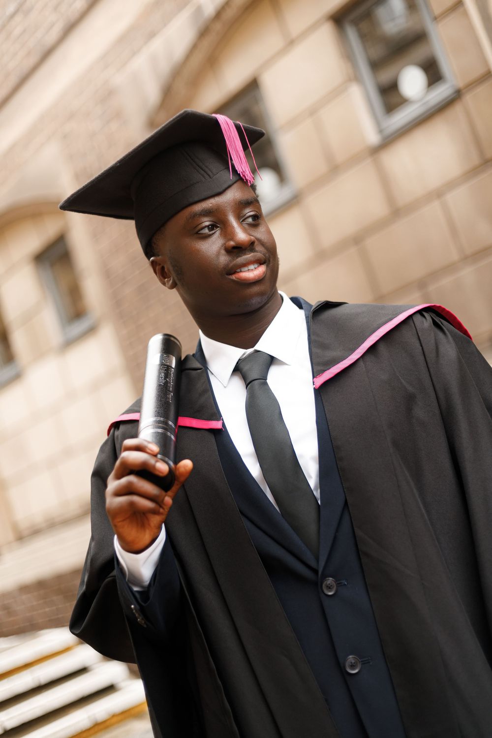 Graduate in black cap and gown holding a diploma while smiling during commencement ceremony.