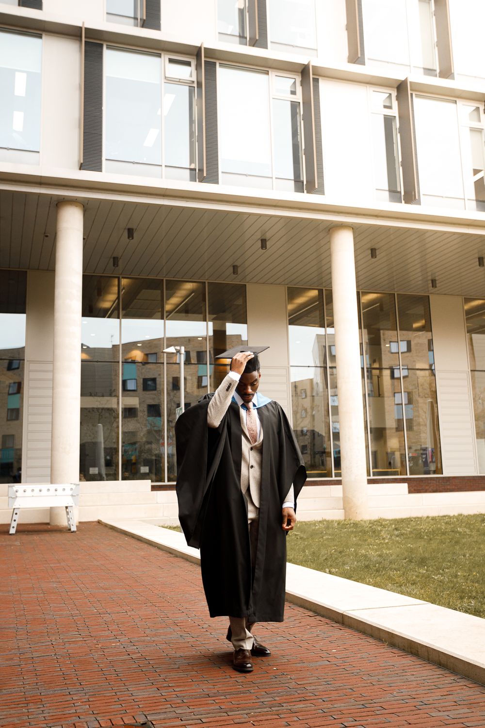 A series of five photos showing graduates in black academic regalia walking along a modern building exterior.