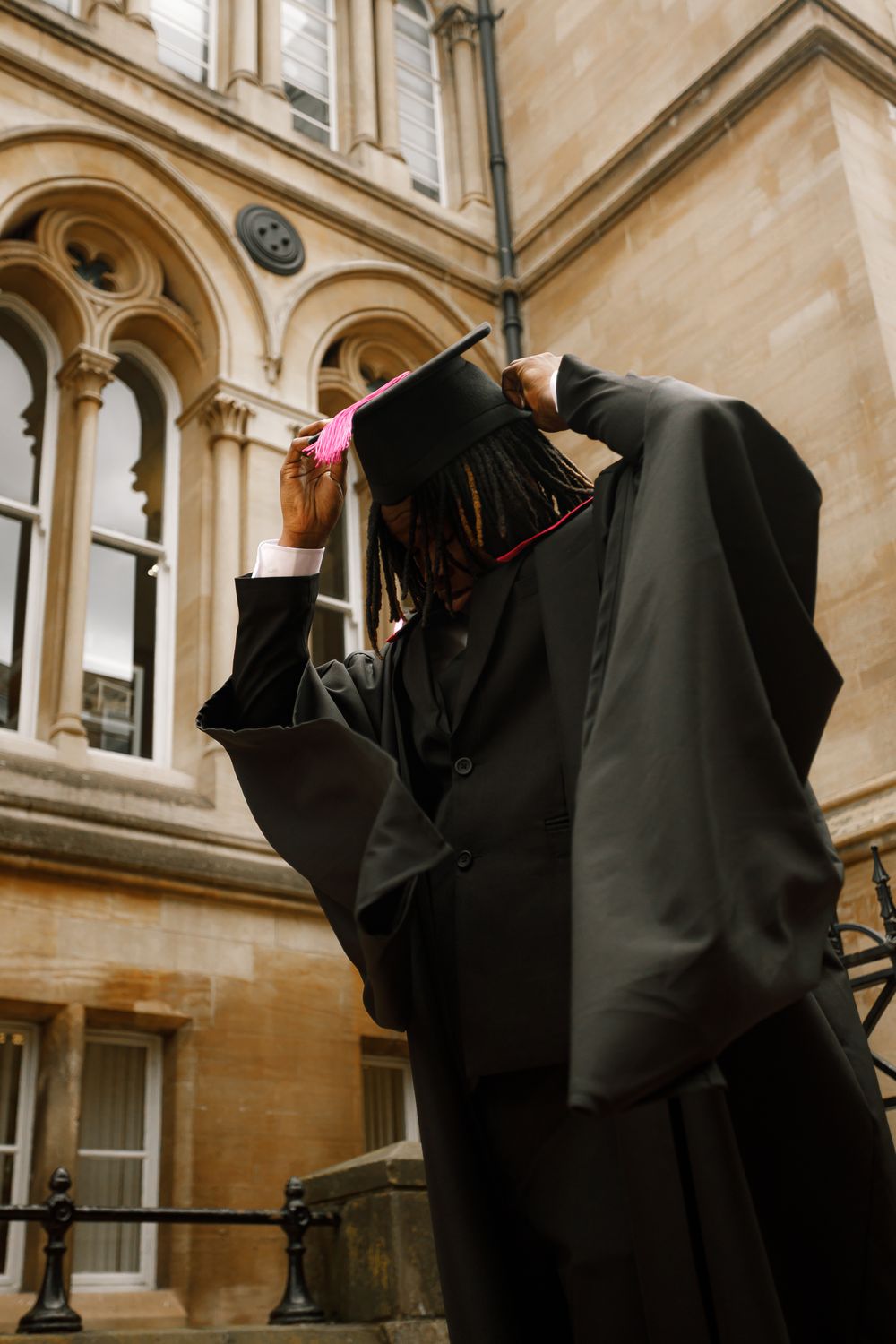 Graduates in black academic gowns and mortarboards gather in a historic stone courtyard during commencement ceremonies.
