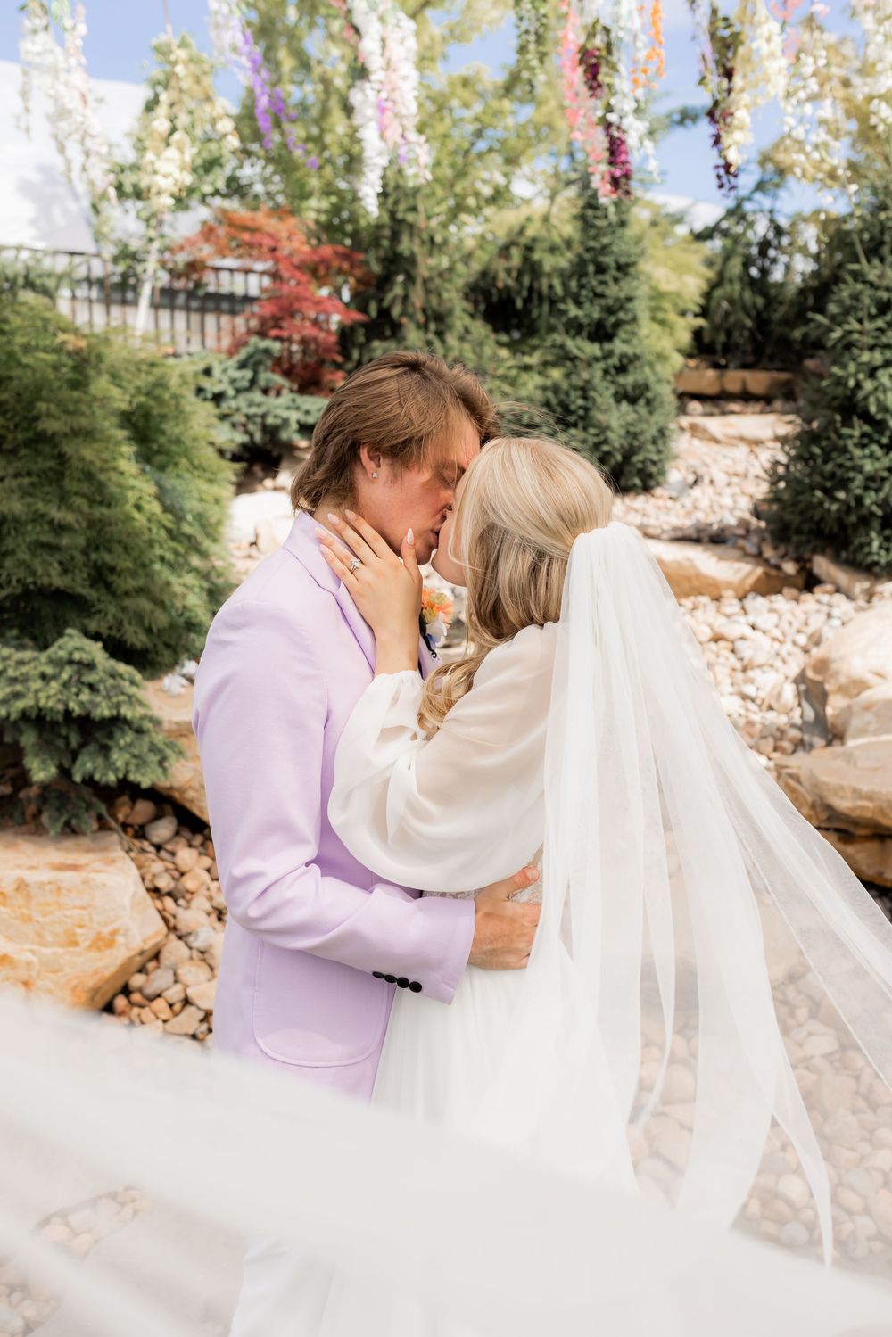 Bride and groom sharing a kiss during a Utah garden wedding, veil flowing in the wind