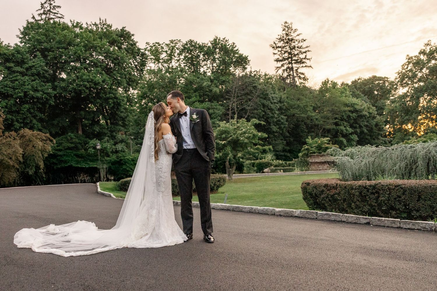 Couple sharing a romantic moment in a sunlit garden with stone wall and lush greenery in the background.