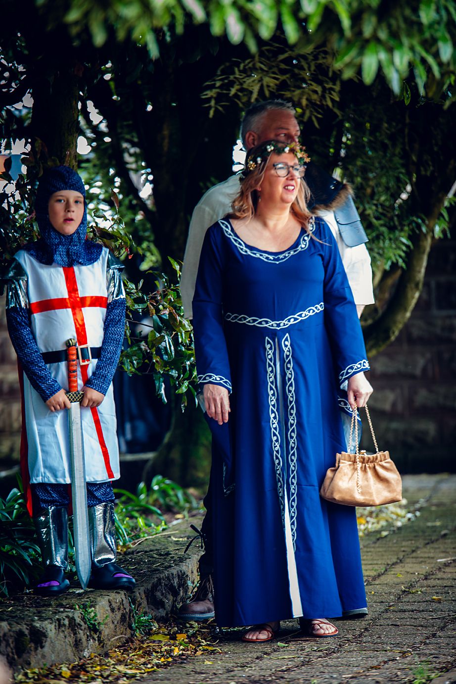 People wearing traditional blue and white religious garments walk along a stone path under green foliage.