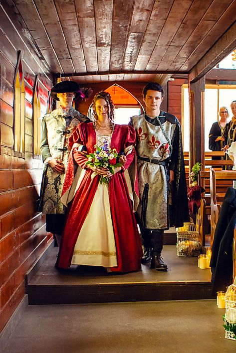 People in medieval period costumes stand inside a wooden-paneled corridor of what appears to be a historic ship or vessel.