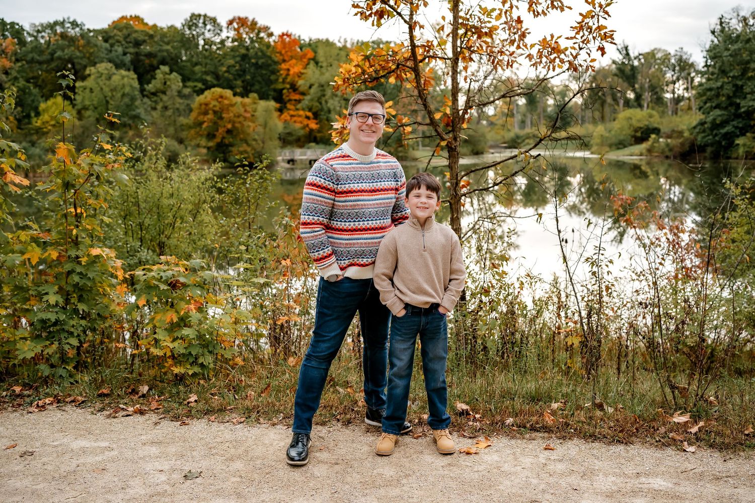 Family walking together on nature path surrounded by autumn trees and water.