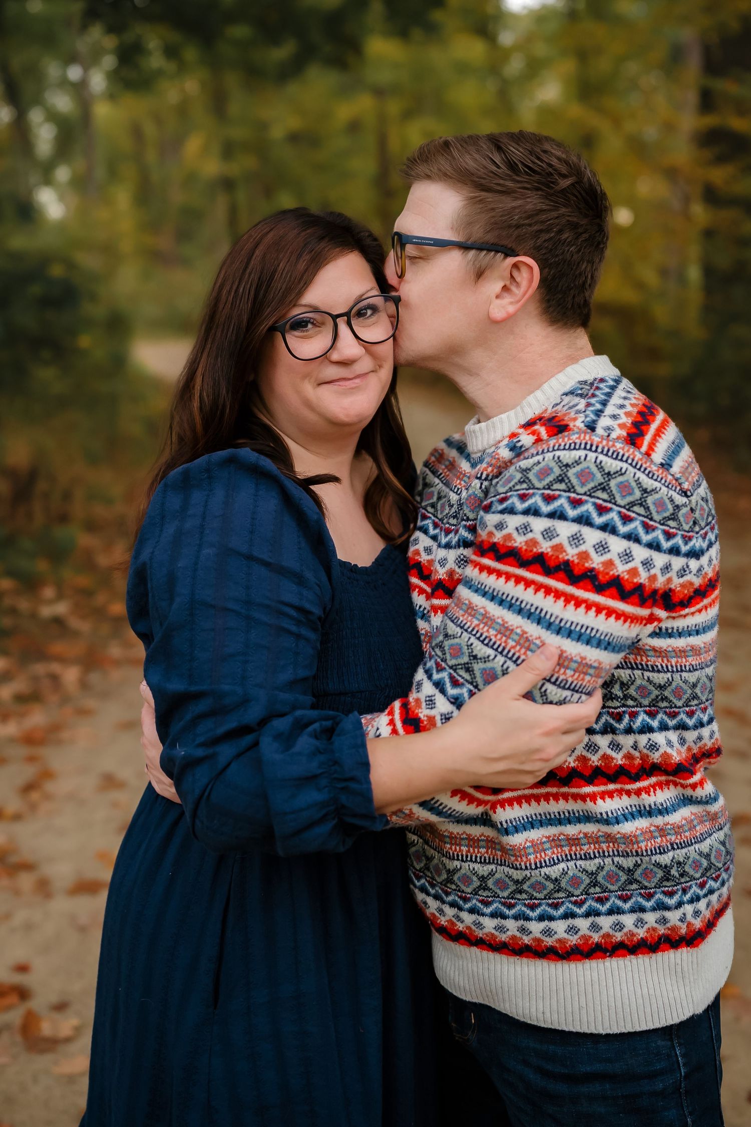 Couple embracing outdoors wearing cozy winter sweaters against natural fall backdrop.
