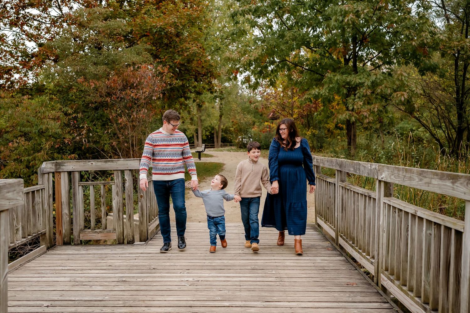 Family walking together on a wooden boardwalk through autumn trees and nature during a fall day.