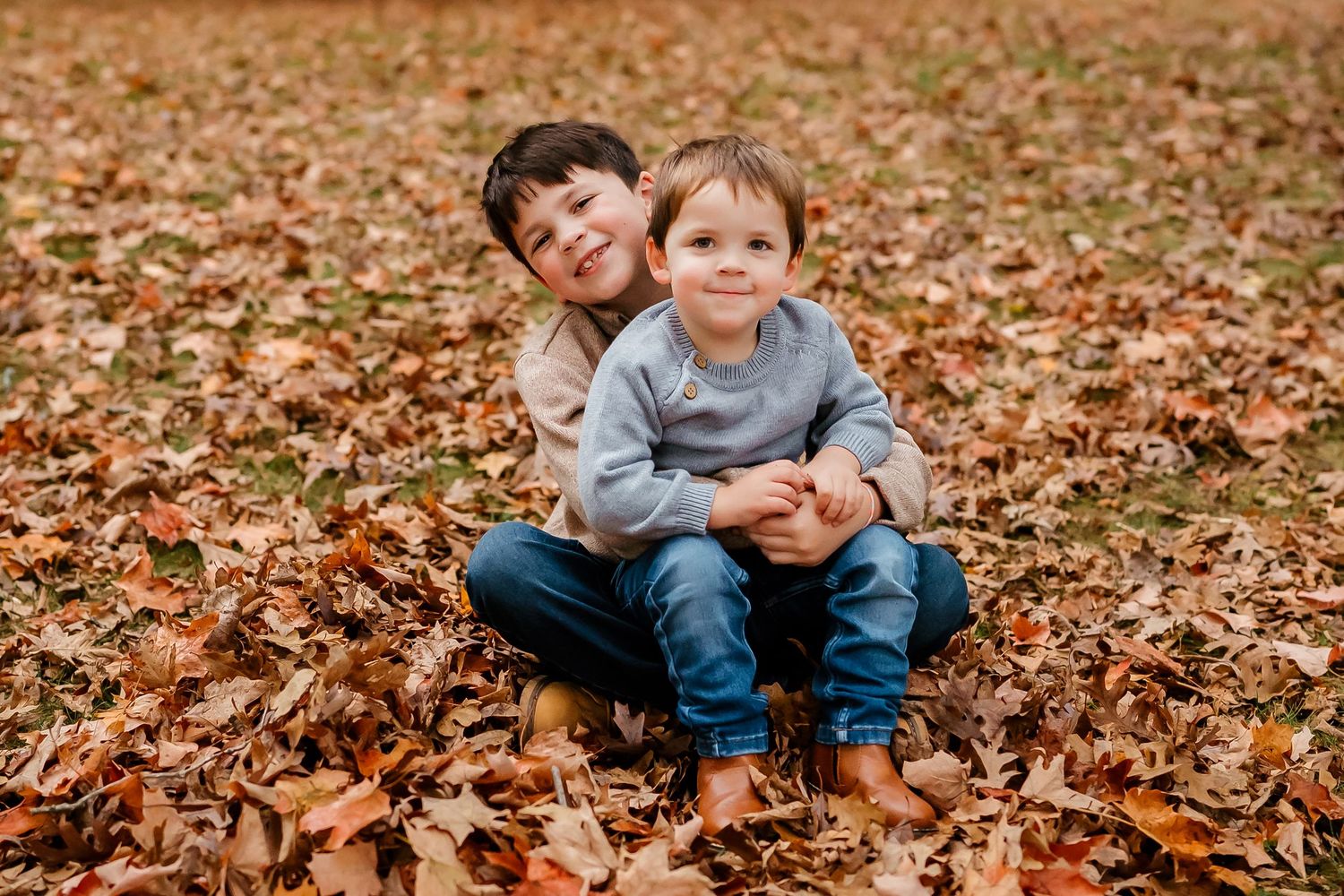 Children playing together in a pile of fallen autumn leaves during a fall photoshoot outdoors.