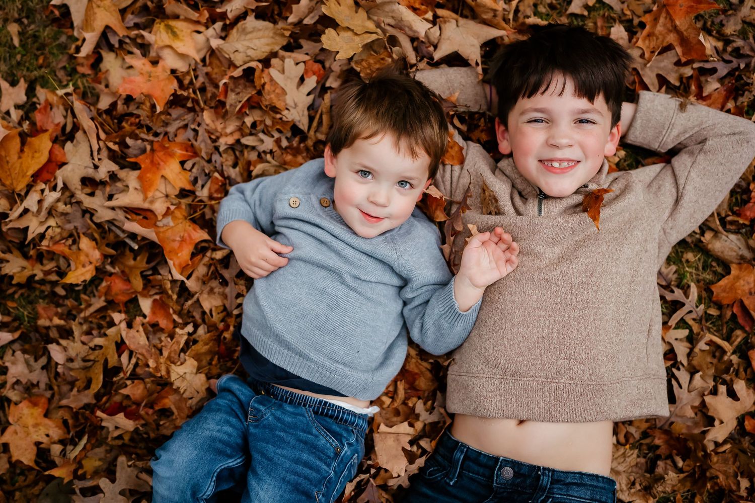 Two children playing and laughing together in a pile of autumn leaves on a sunny fall day.