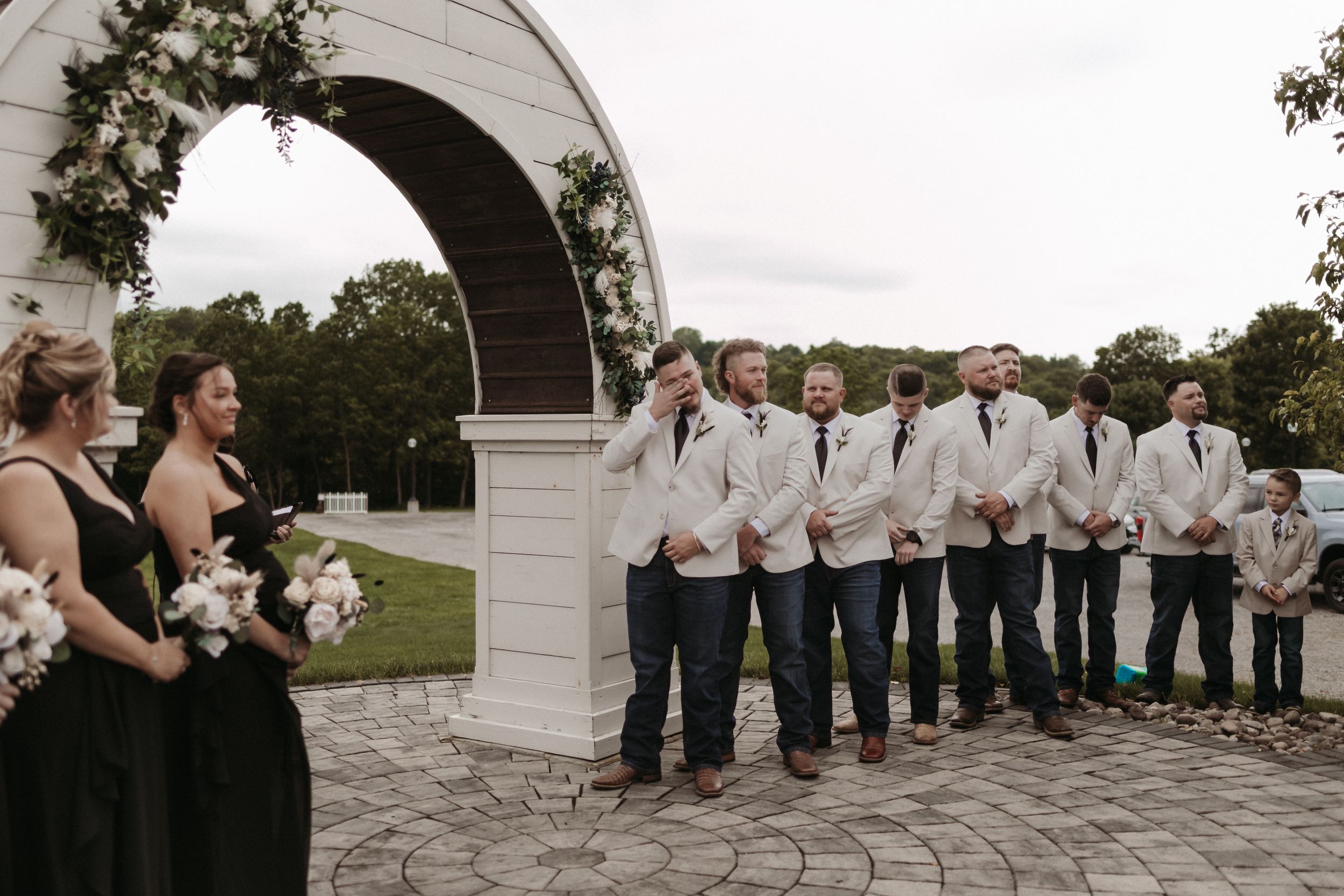 Wedding party members line up in front of a white gazebo during an outdoor ceremony.