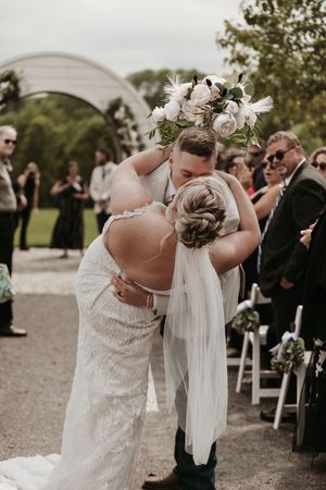 A wedding ceremony moment showing an embrace under an arch with guests watching.