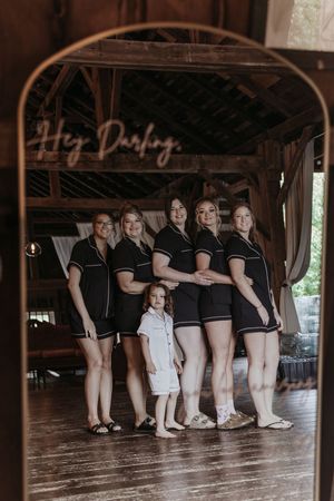 A group wearing matching black outfits and white shoes sits in a rustic wooden barn venue for a casual photo.