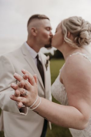 A romantic wedding couple sharing a kiss while holding hands, with the bride's engagement ring prominently displayed.