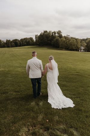 A bride and groom walking hand in hand across a green field on their wedding day.
