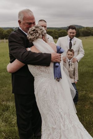 Wedding party gathers for emotional moments on a green hillside.