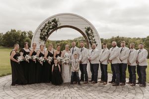 A wedding party in formal attire poses together on a stone patio during an outdoor celebration.
