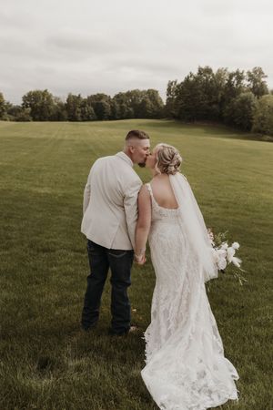 A wedding couple sharing an intimate moment in a scenic field with the bride holding a white bouquet.