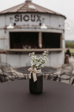 Mason jar centerpiece with white flowers against rustic Sioux building backdrop.