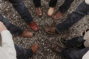 Close-up shot of various dress shoes and boots on gravel ground.
