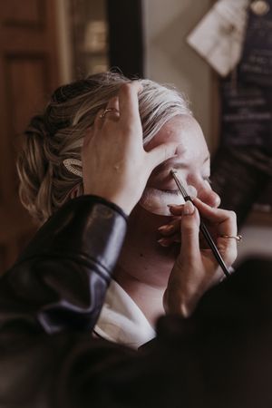 Close-up shots of someone getting makeup professionally applied in warm lighting.