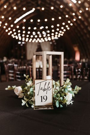Wedding reception table decor featuring Table 19 sign in a lantern with string lights overhead.