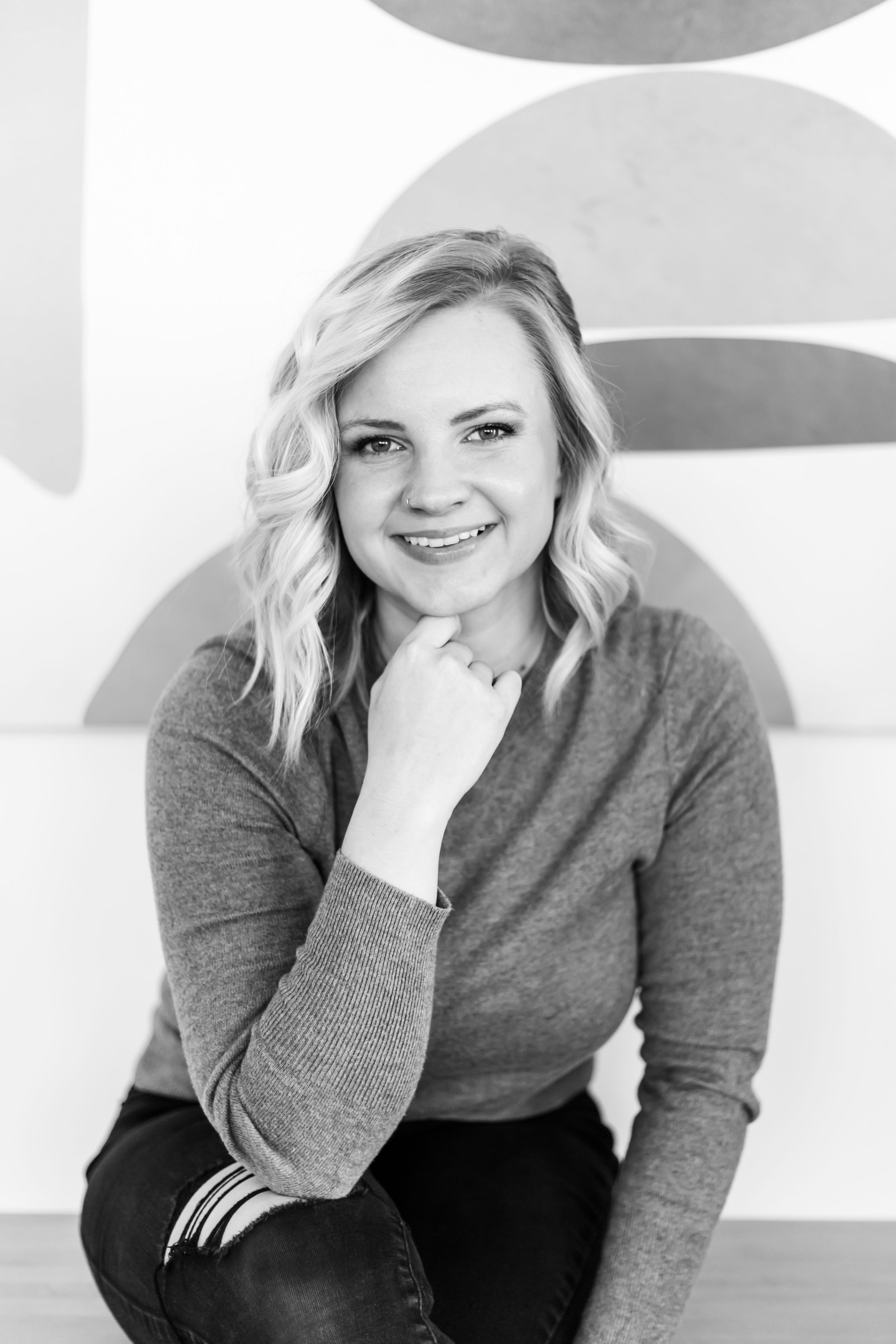 Professional headshot portrait of someone in a gray sweater with a bright smile against a white background.