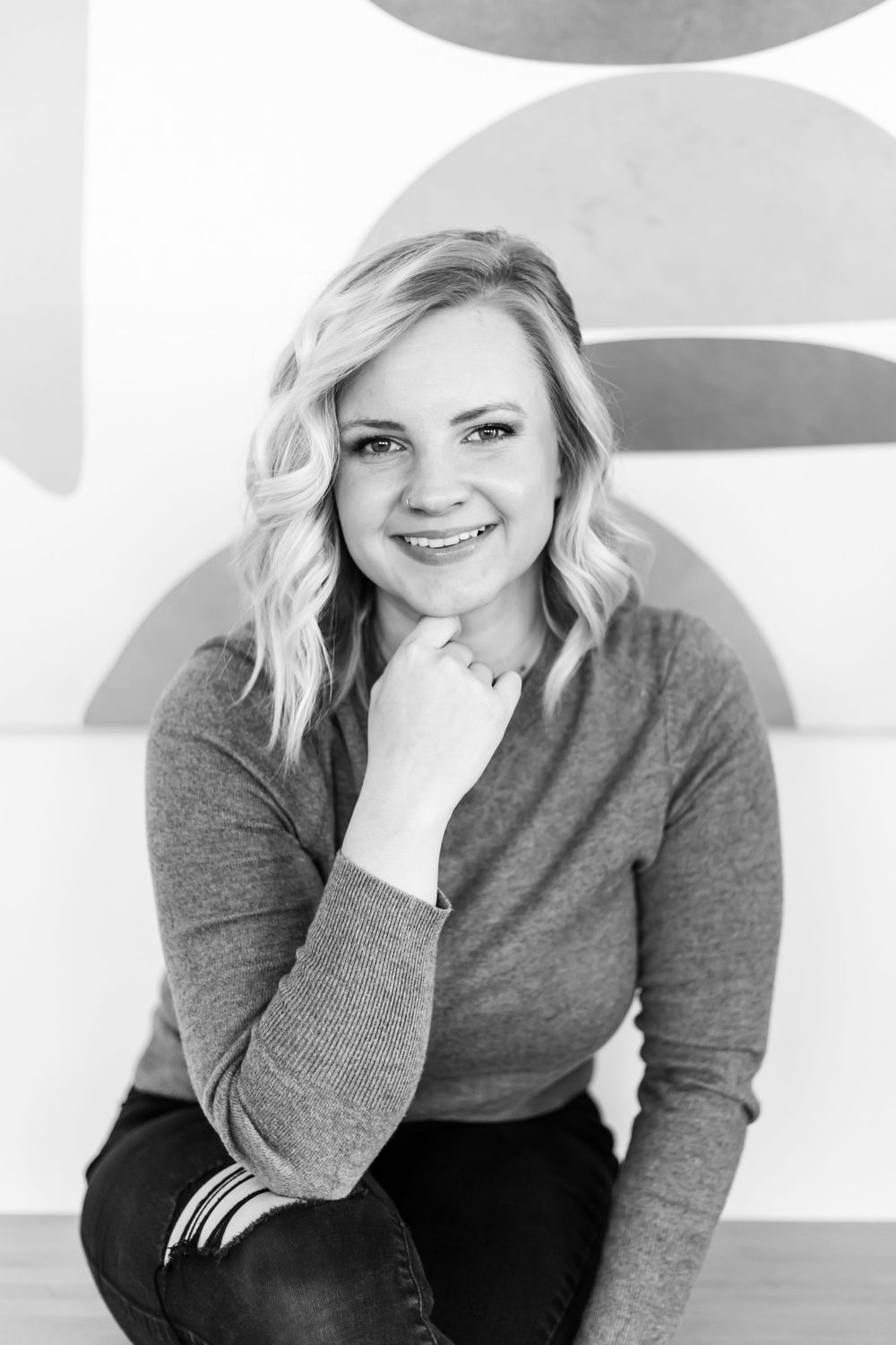 Professional headshot portrait of someone in a gray sweater with a bright smile against a white background.