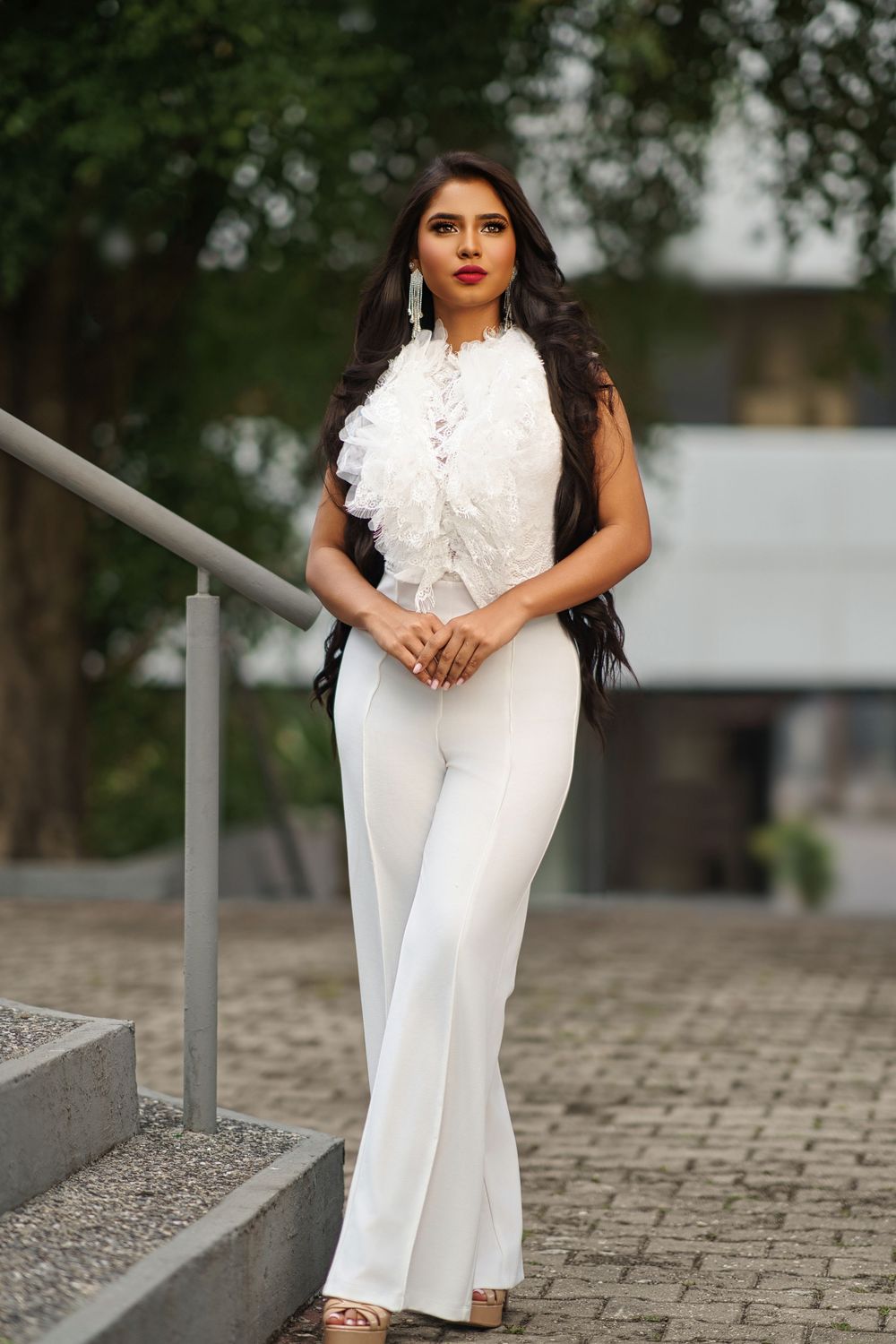 A figure in an elegant white jumpsuit poses on stone steps with a ruffled collar detail.