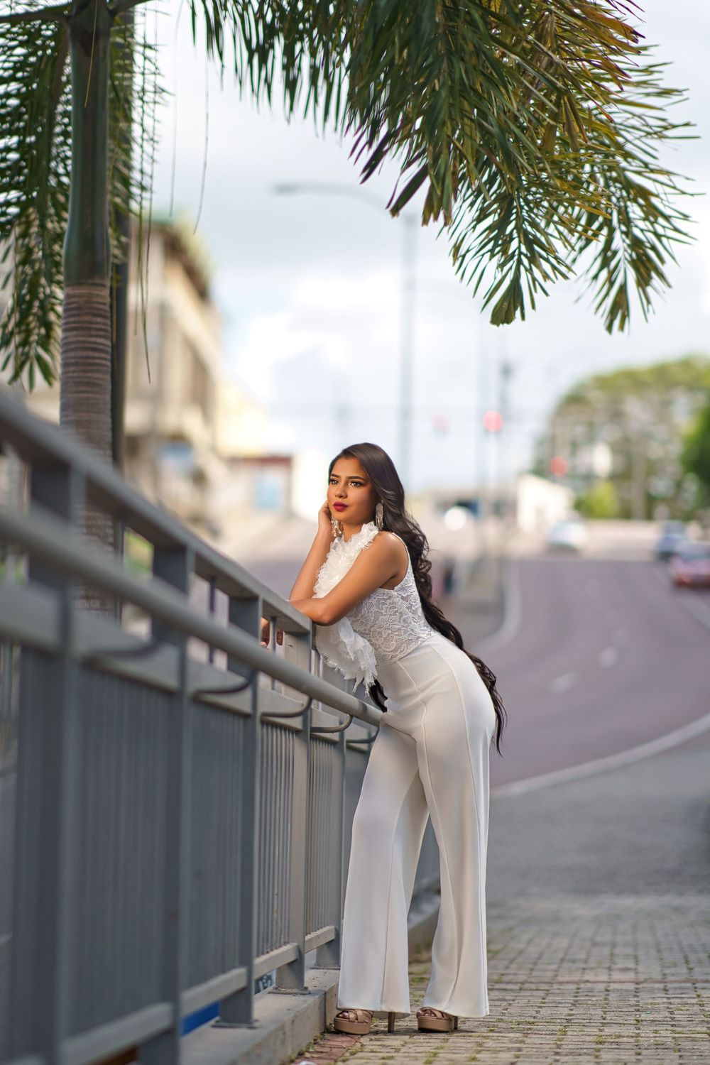 Person in white outfit stretches against railing along palm tree lined walkway during outdoor workout session.