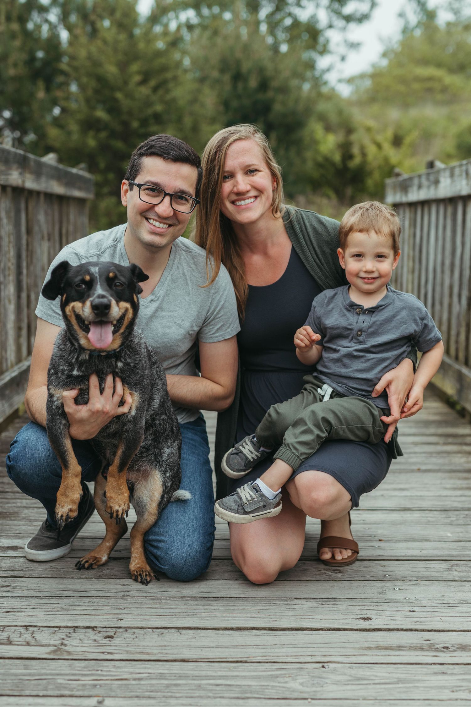 Happy family portrait on wooden boardwalk with their smiling dog creating casual outdoor scene.