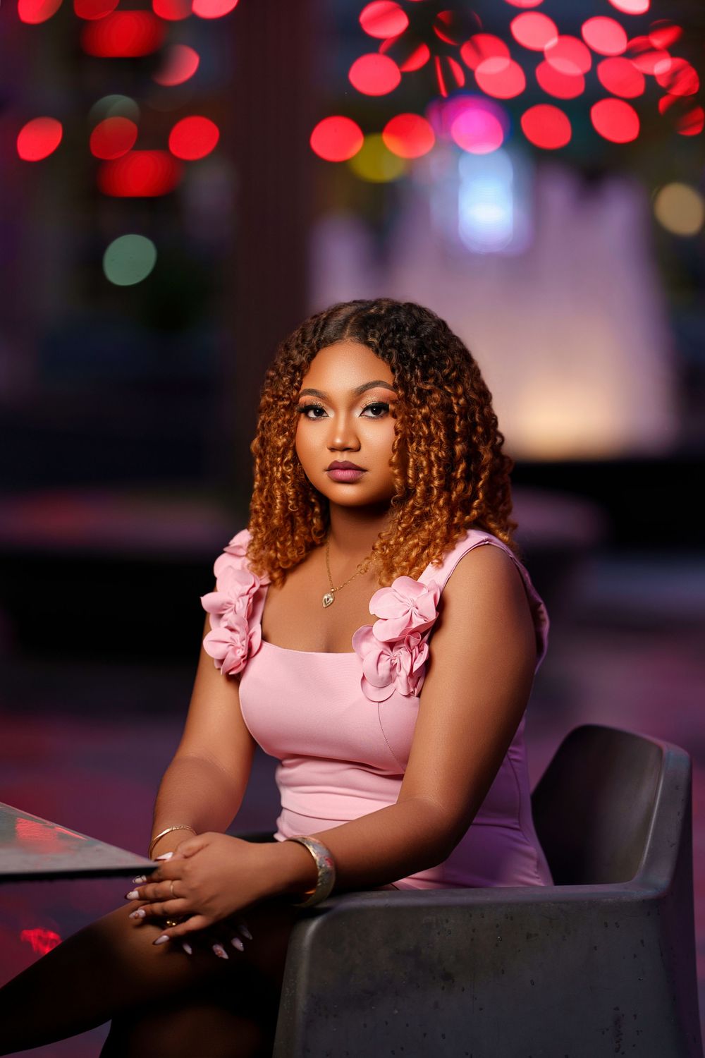 Portrait session with soft pink dress against blurred bokeh background with red and green lights.