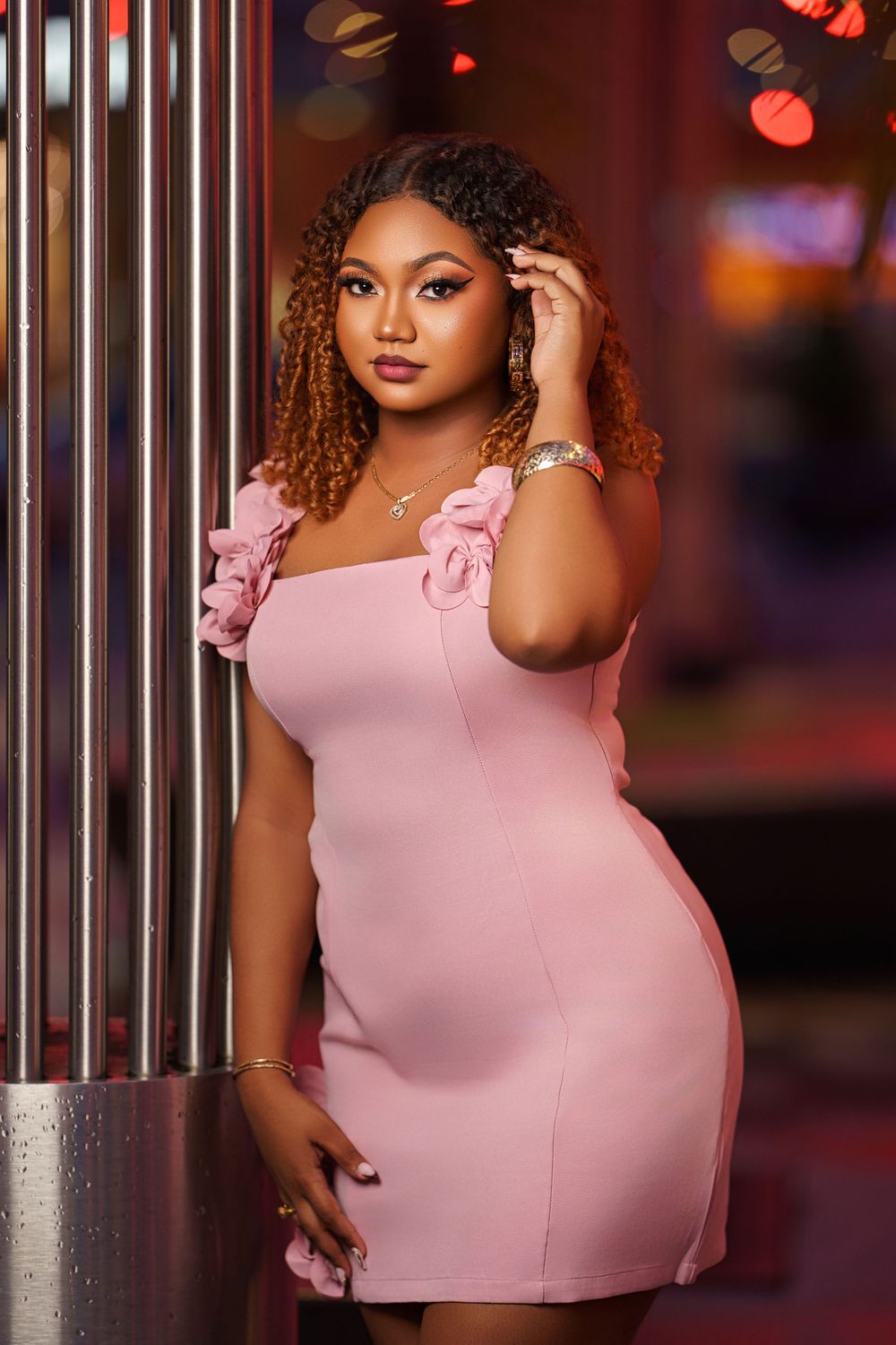 Stylish pink dress with ruffle details photographed against industrial columns and ambient lighting.