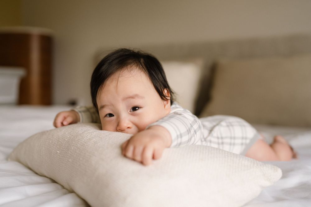 Baby rests peacefully on white bedding in soft natural light.