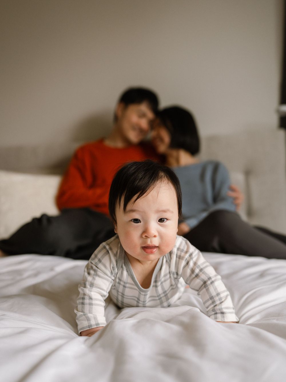 A sequence of photos showing a baby in white clothing smiling and playing on white bedding.