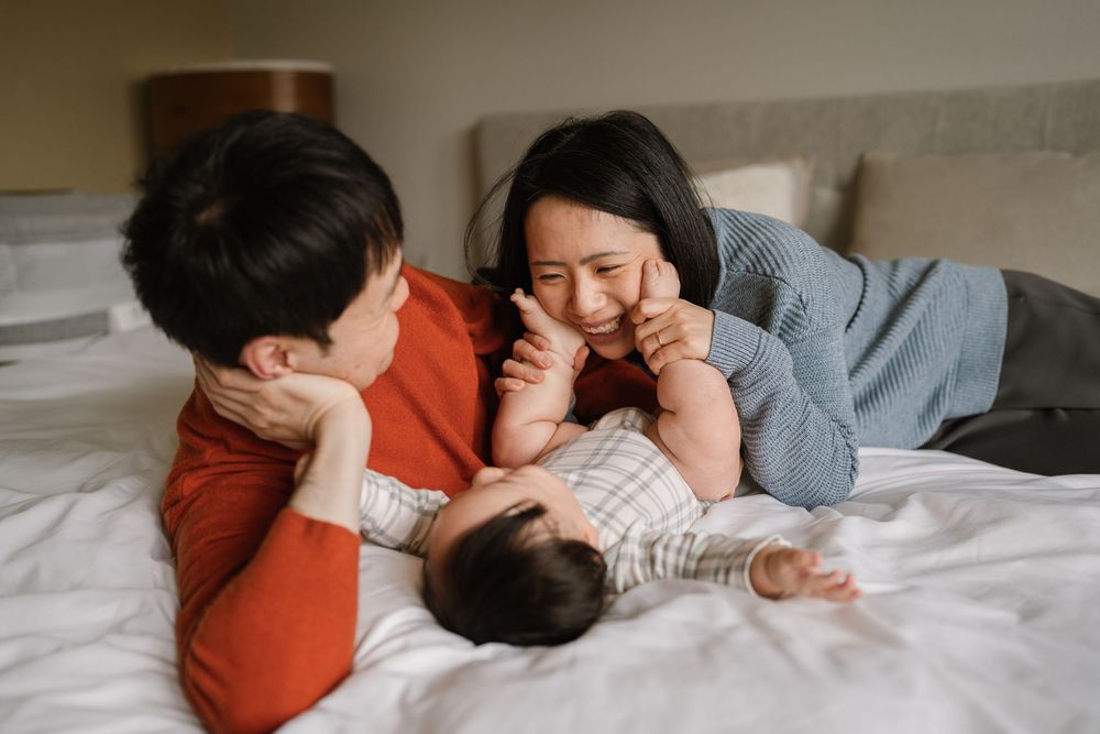 A family enjoying playful moments together while lying on white bedding.