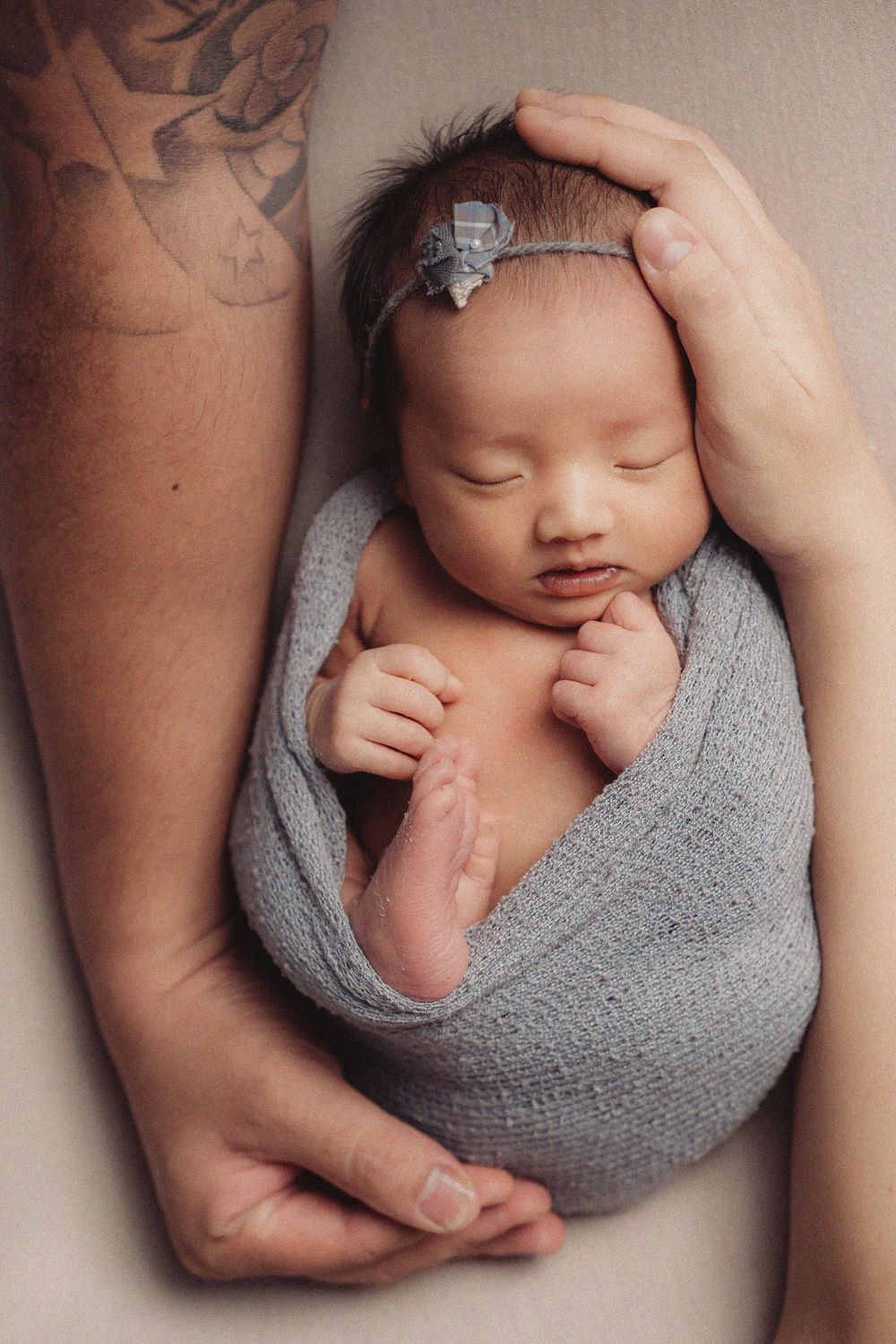 Newborn baby wrapped in gray knit blanket with gentle hands supporting in artistic portrait series.