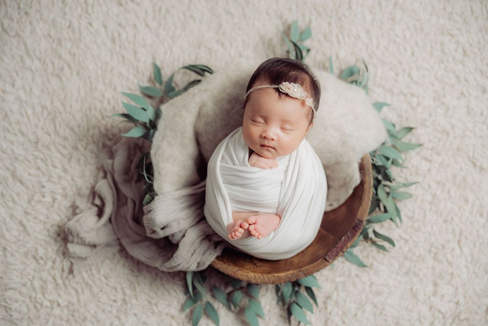 Sleeping newborn posed on white textured surface with eucalyptus leaf accents.