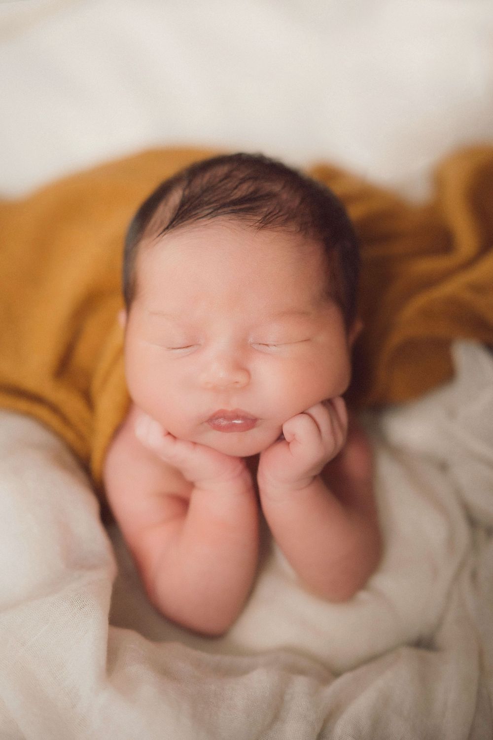 Sleeping newborn baby with closed eyes on cream bedding with golden brown accents.