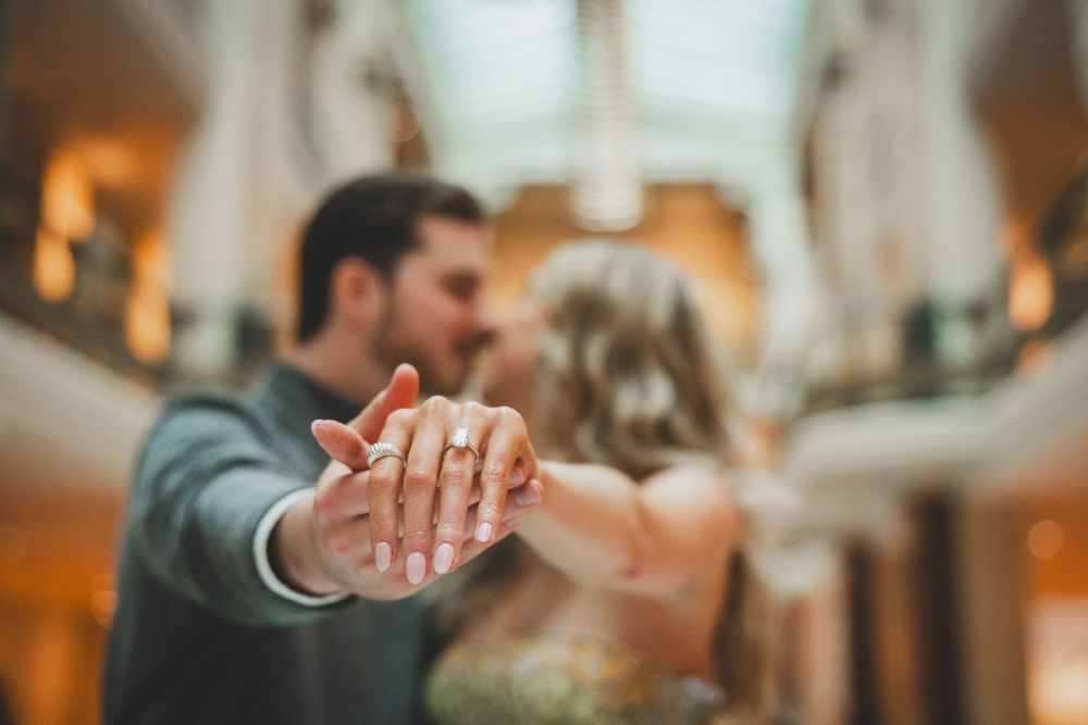 Close-up of hands holding each other in a romantic gesture with warm lighting and blurred background to show off their new engagement ring