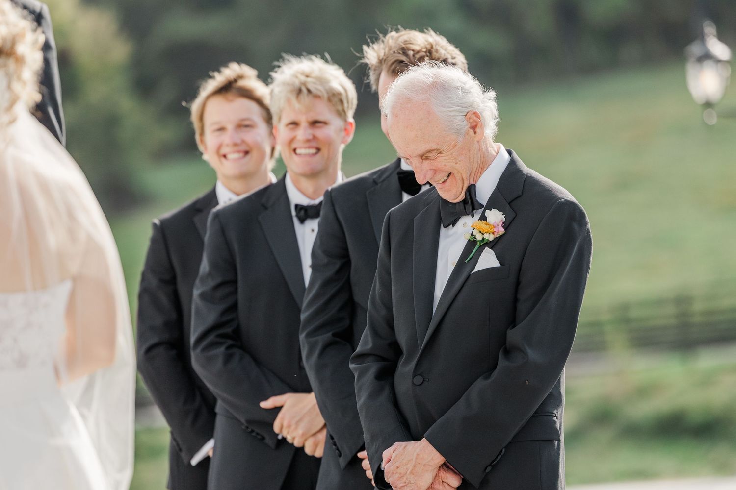 Groomsmen in black tuxedos share a lighthearted moment during wedding ceremony photos.
