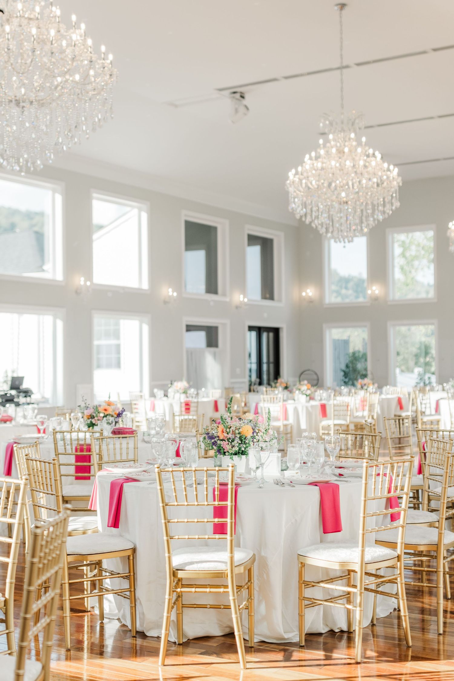 Elegant wedding reception hall with crystal chandeliers, gold chairs, and white table settings.