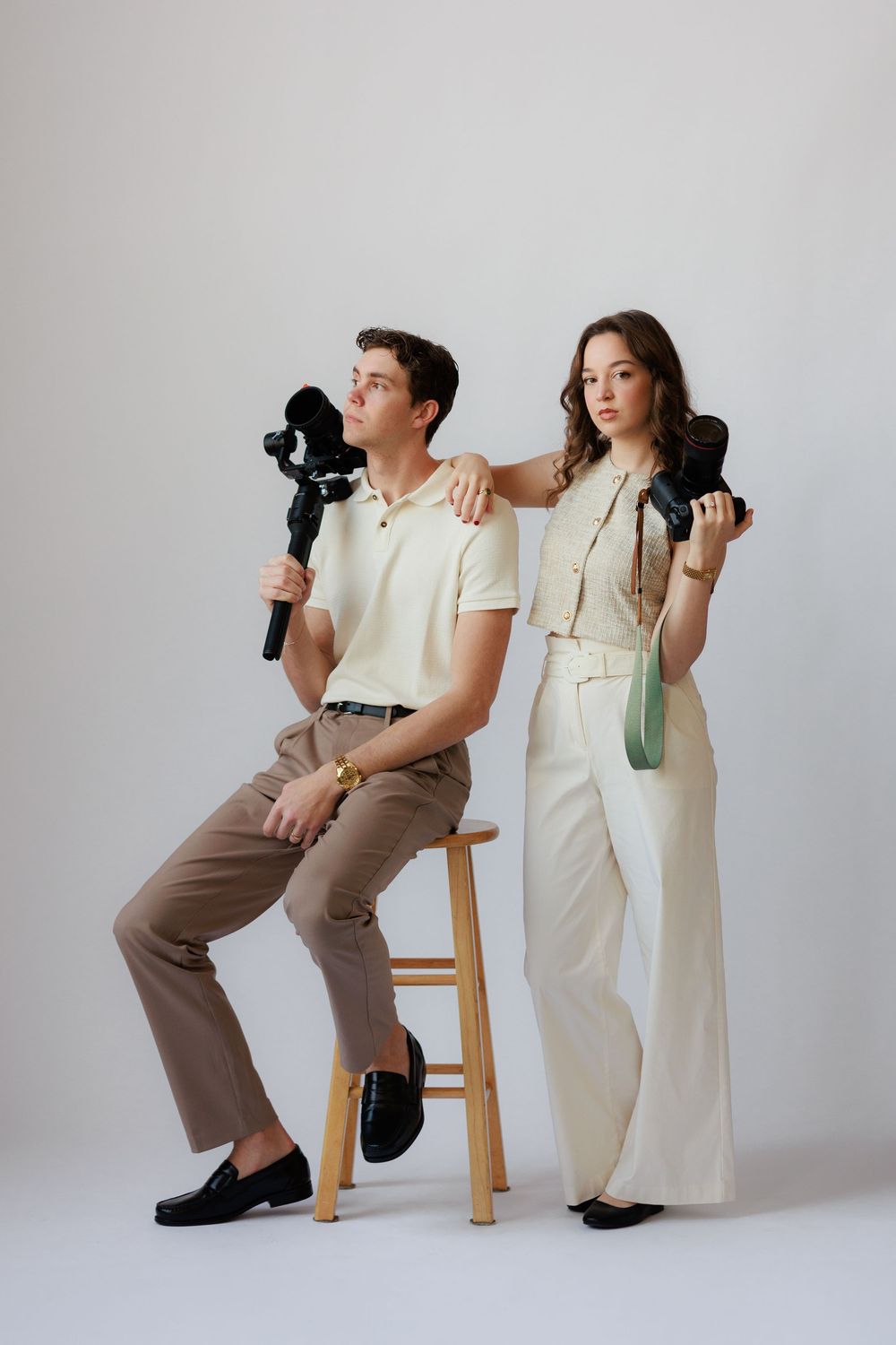 Two photographers in contrasting outfits pose with cameras against white backdrop in artistic composition series.