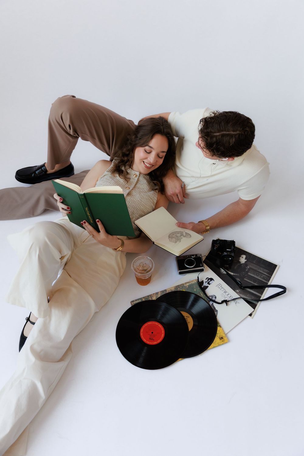 Person in white loungewear relaxing on floor while listening to vinyl records on turntable in minimalist setting.