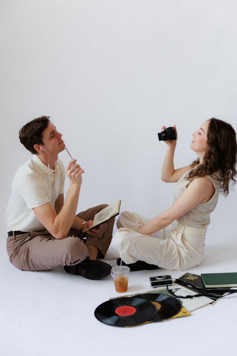 Two people lying on floor back-to-back listening to vinyl records and reading books in a minimalist setting.