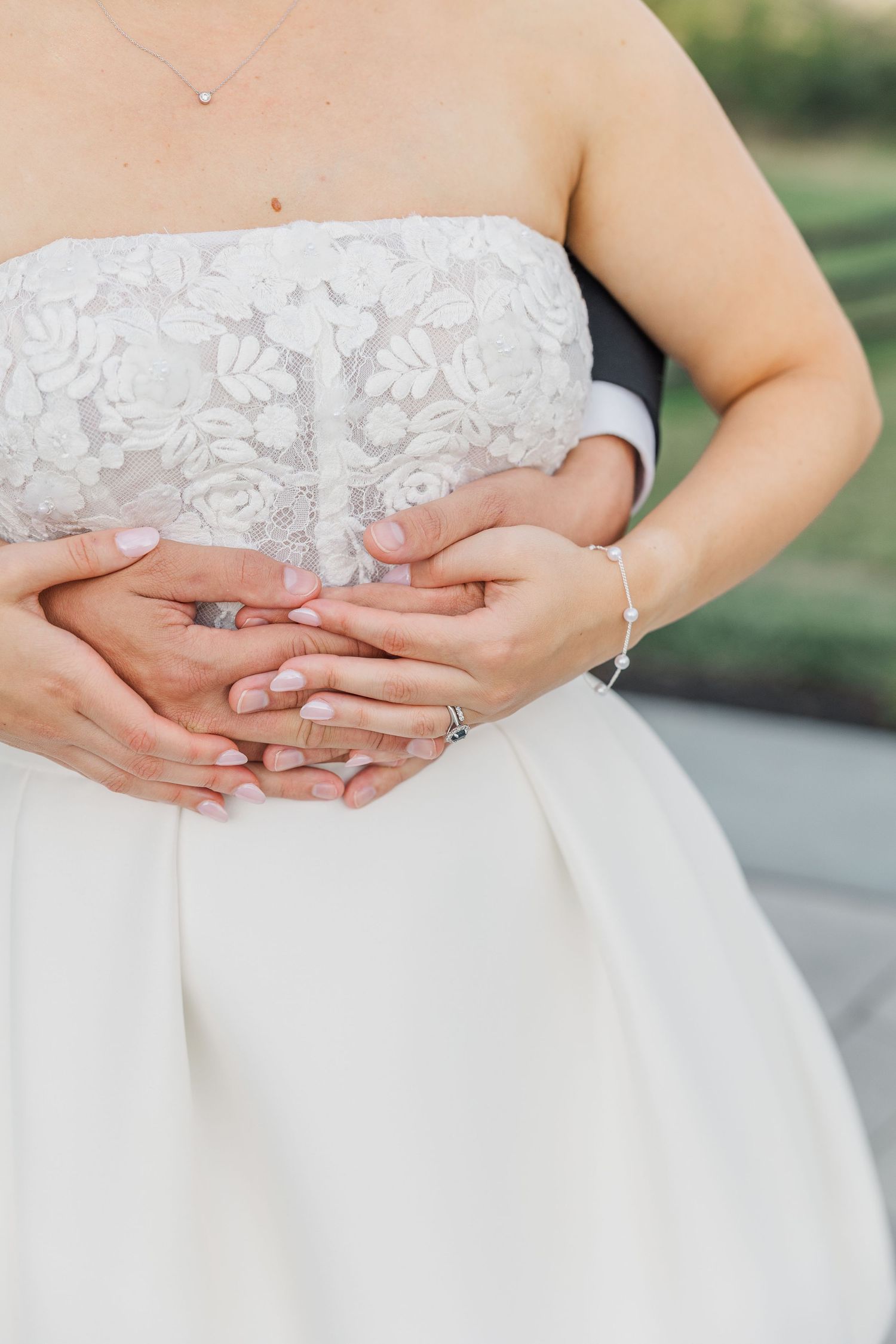 Close-up of delicate lace details and hands with wedding rings against a white dress.