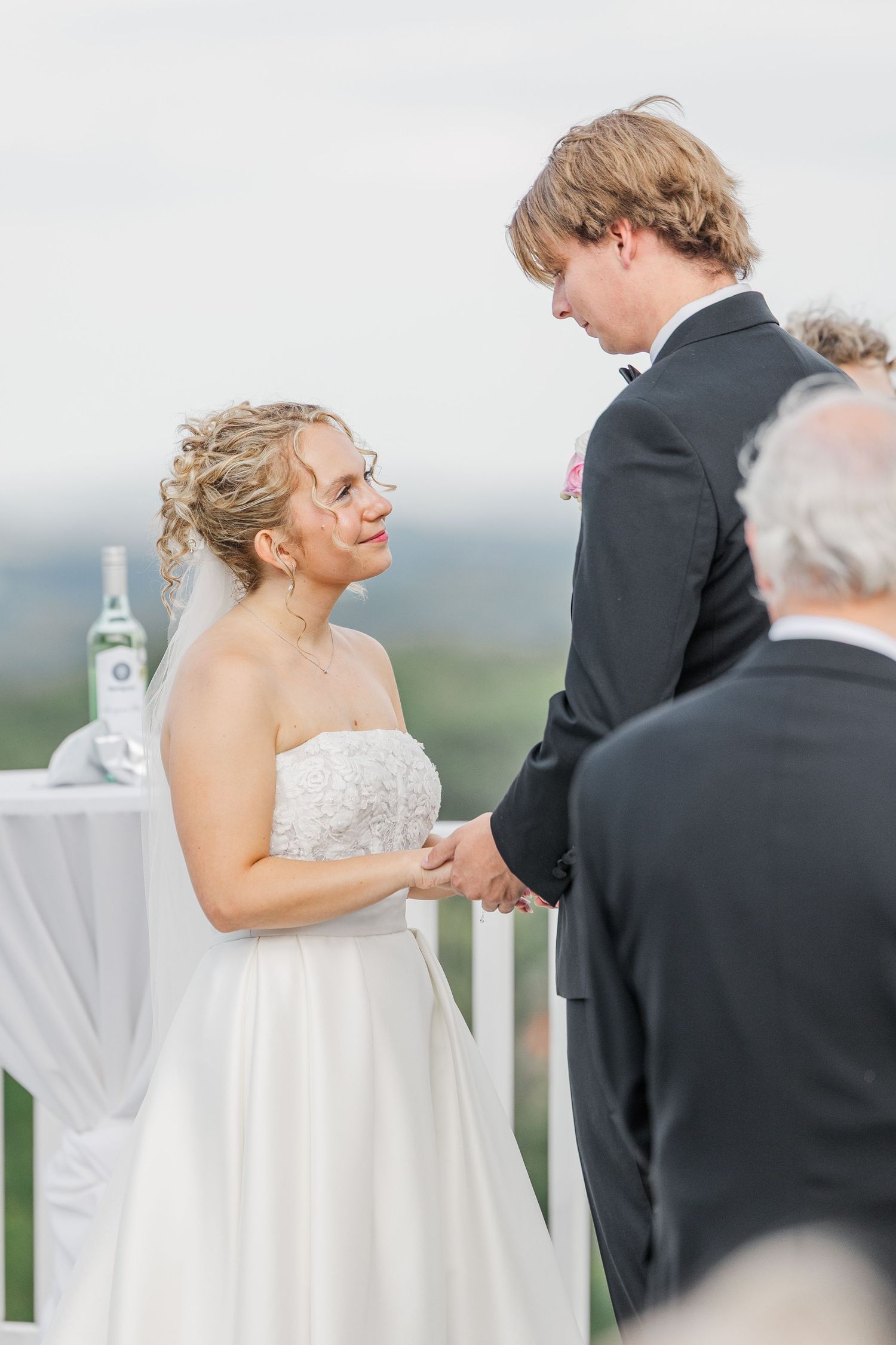 A romantic wedding ceremony moment captured on a scenic outdoor terrace with white decor and mountain views.