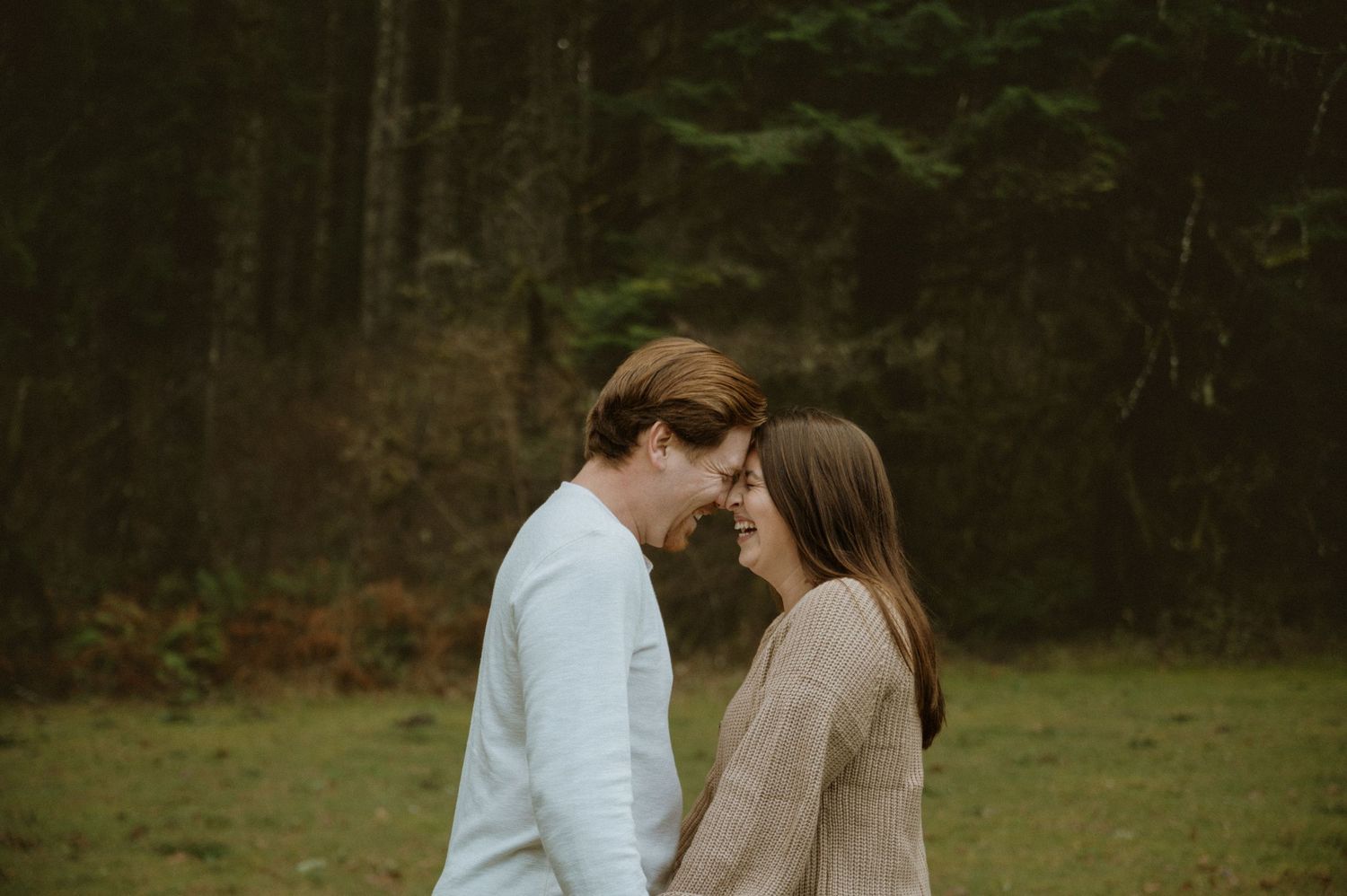 A couple shares a romantic moment in a scenic outdoor setting with trees and natural lighting.