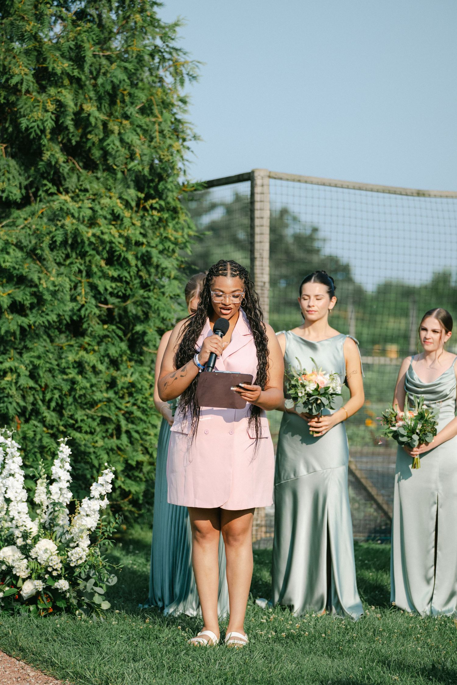 Wedding party poses in pastel bridesmaid dresses against lush green foliage and white flowers in an outdoor garden setting. - Elawa Farm
